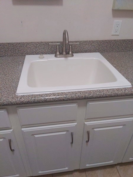 Newly installed sink on granite countertop with white cabinets.