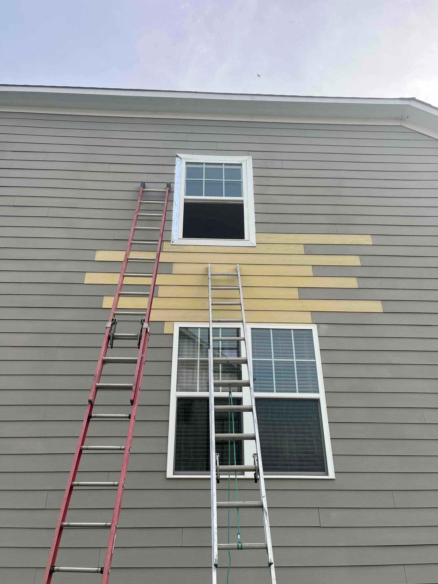 Siding and window replacement in progress with ladders and new boards installed in Chapel Hill NC by Ace Handyman Services Durham Chapel Hill.