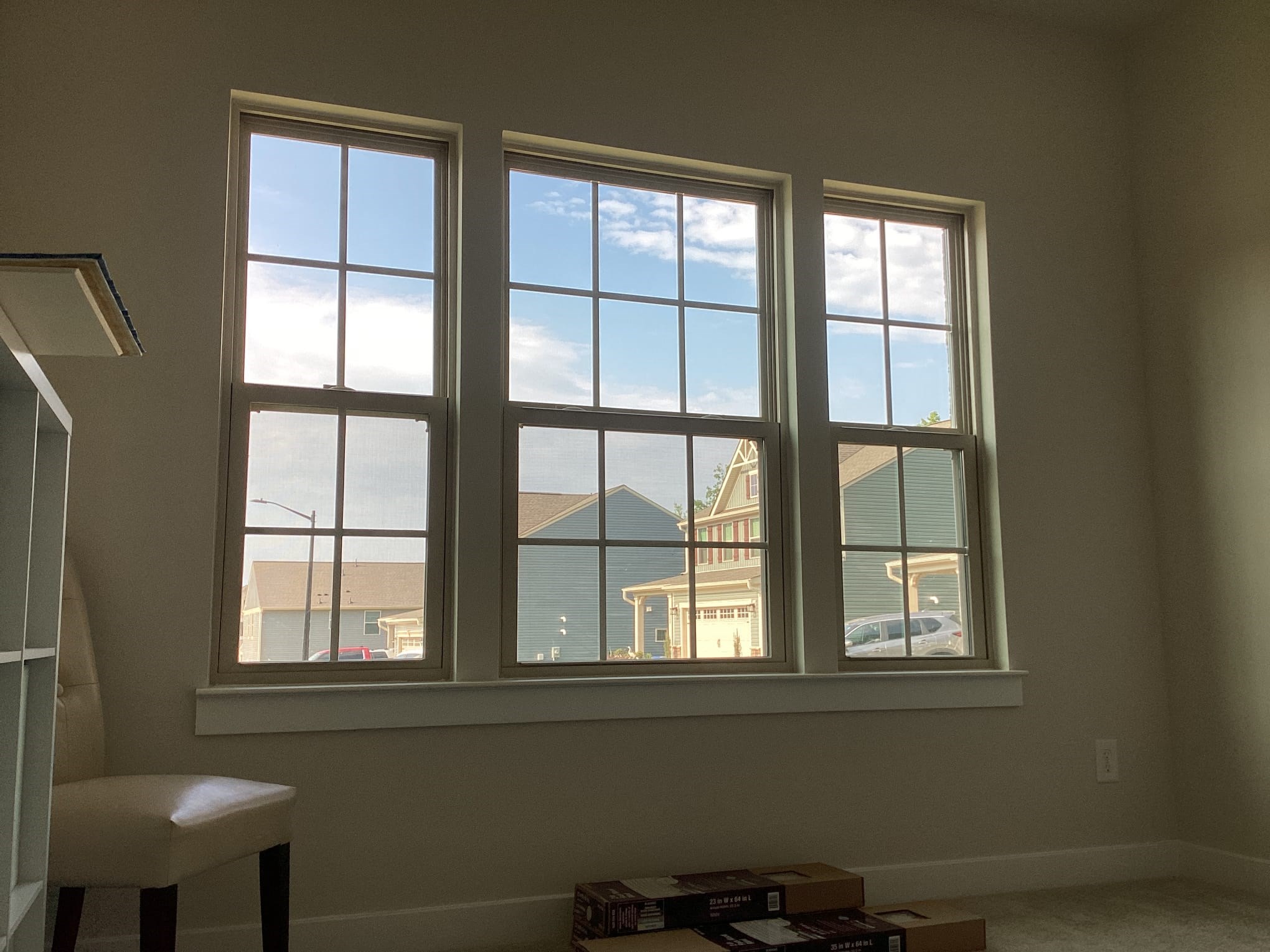 Three large windows overlooking suburban houses, interior view.