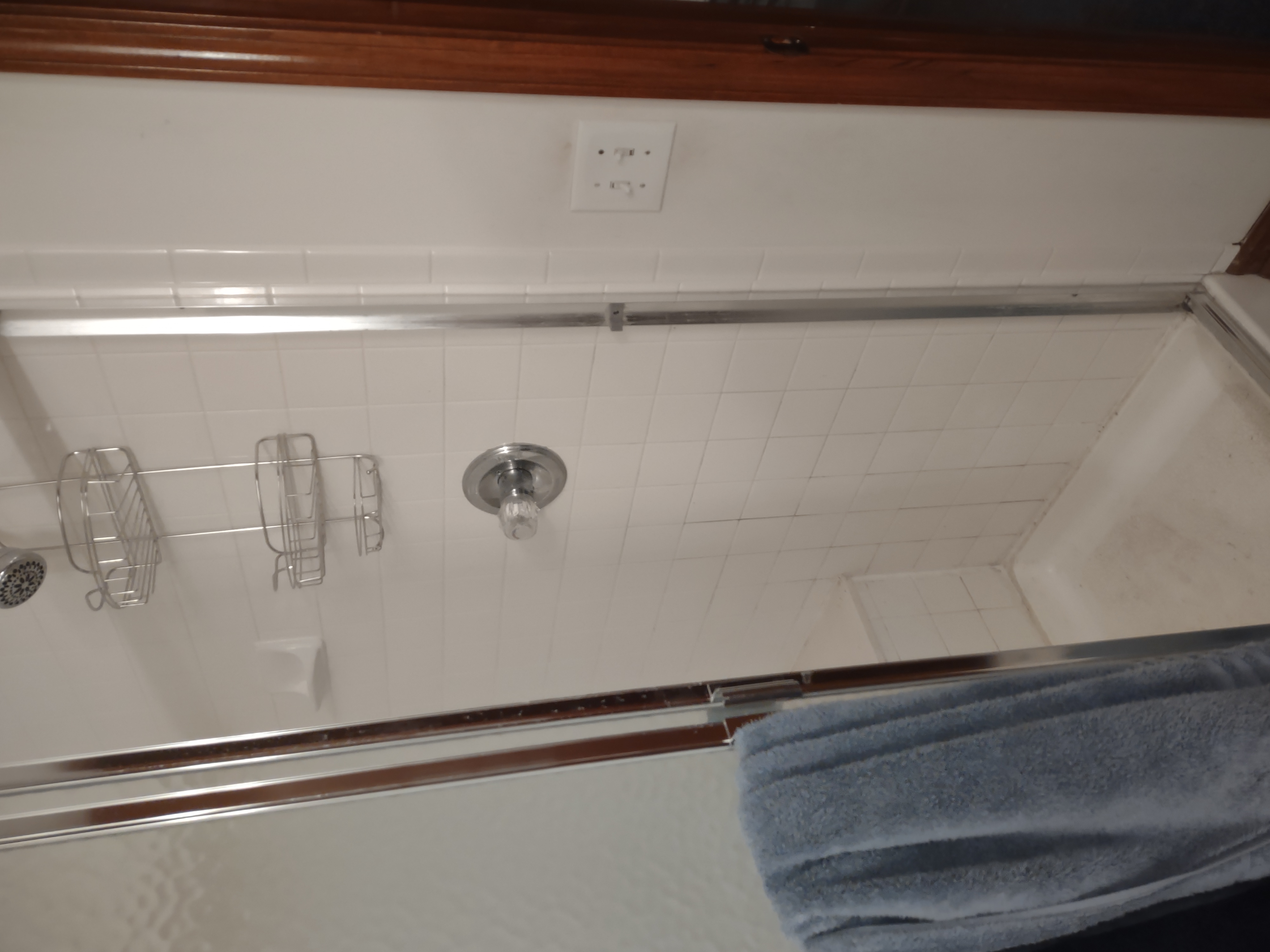 Small white tiled shower with chrome fixtures and blue towel.