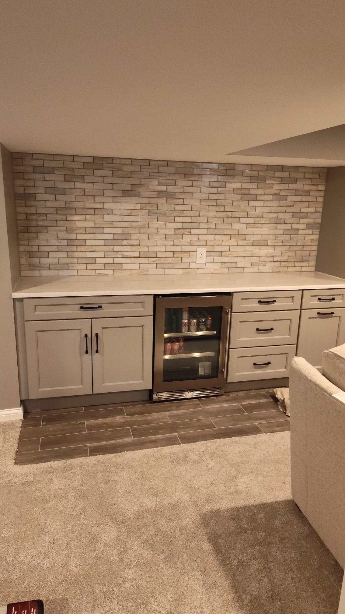 Home bar setup with cabinets and small fridge, tiled backsplash.