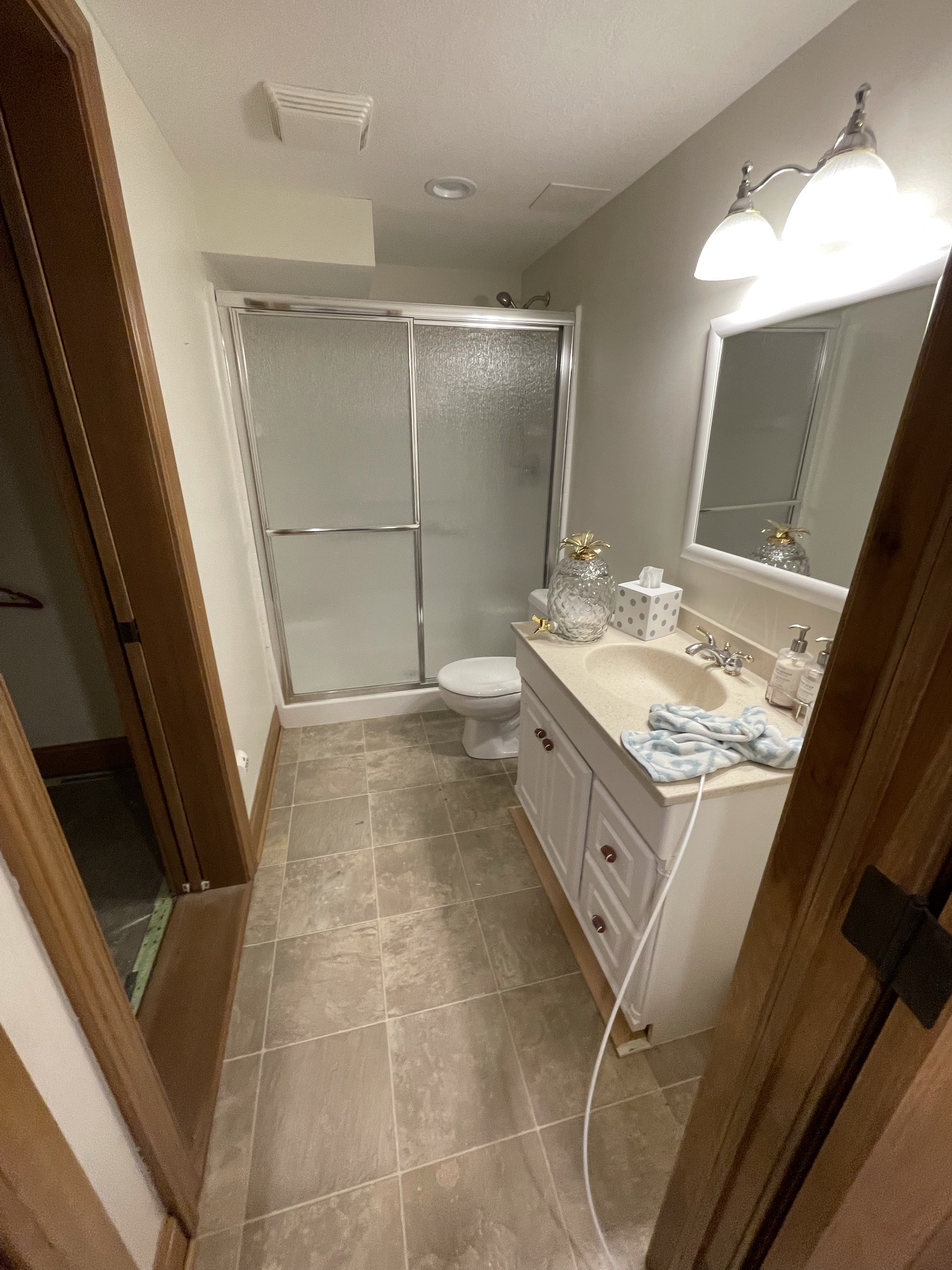 Bathroom with tiled floor, shower, vanity, and bright lighting.