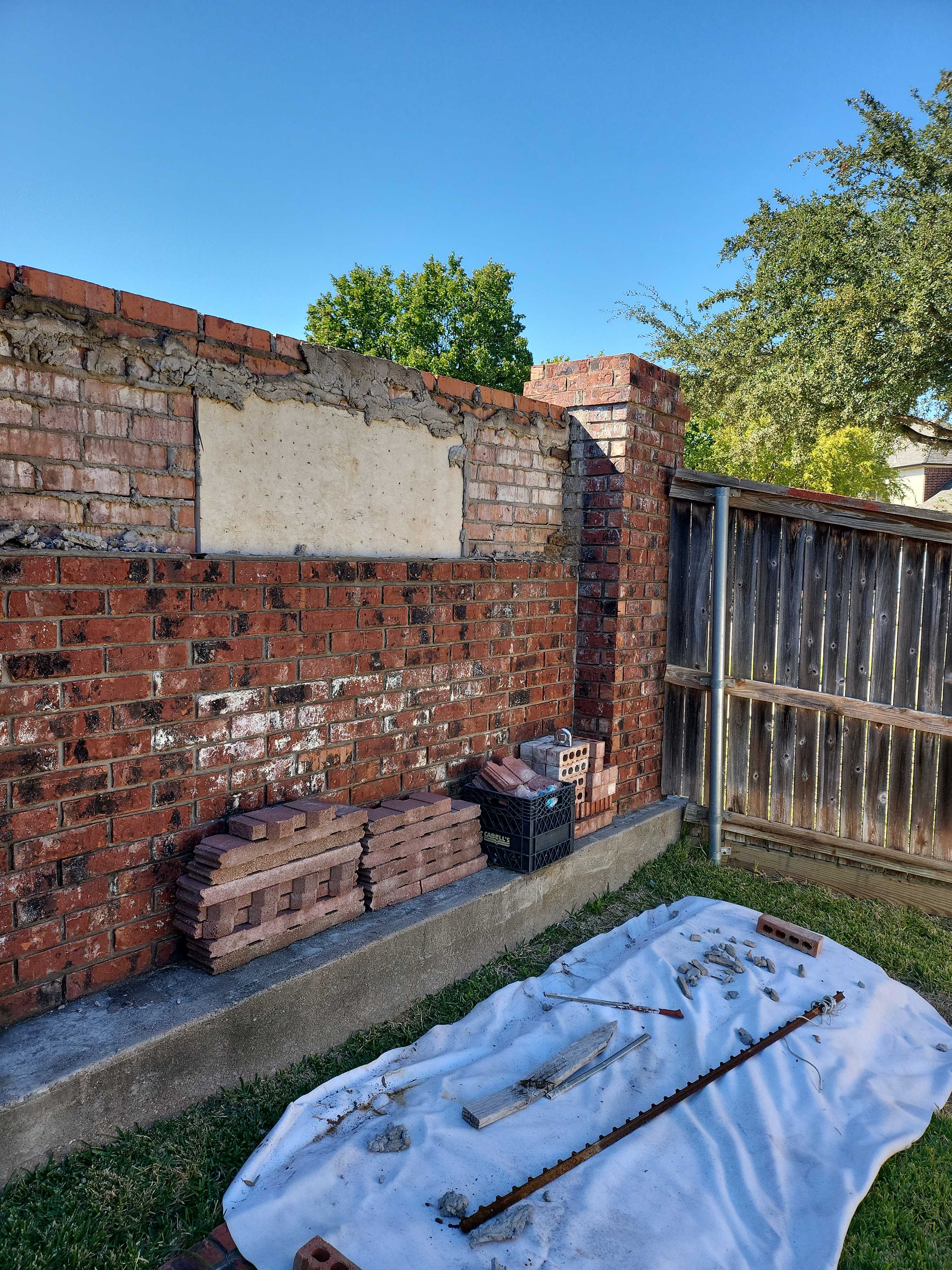 Brick wall repair with tools and materials on a tarp.