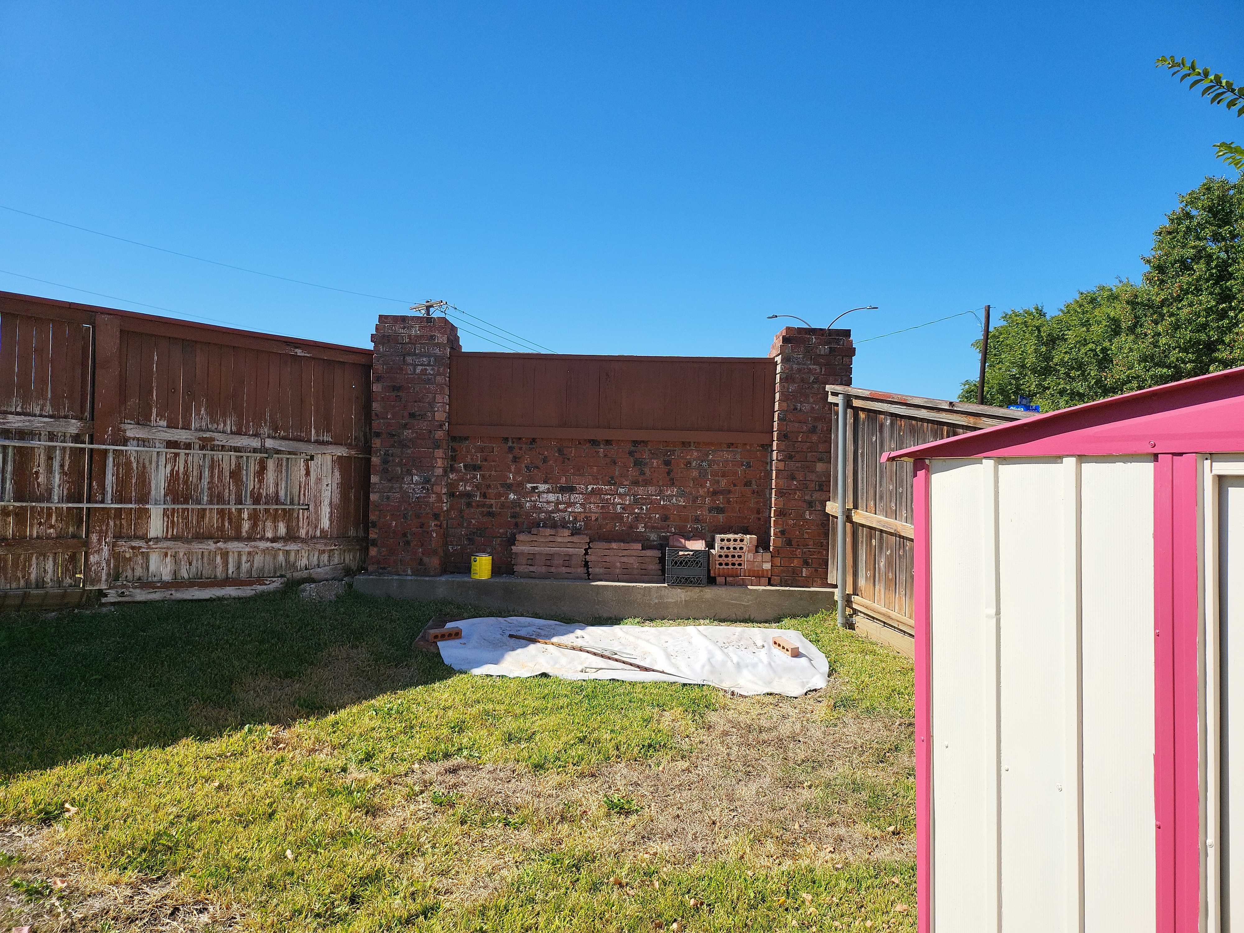Brick wall project setup near fence and pink/white shed.