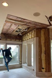 Handyman inspecting exposed ceiling and wall insulation.